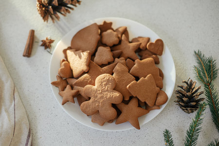 Delicious gingerbread cookies in plate with fir branches, pine cones and napkin on modern countertop...