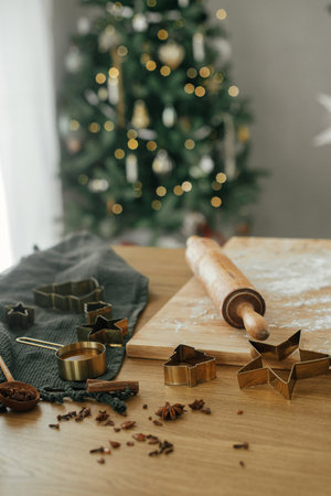 Making christmas gingerbread cookies. Flour on wooden board, rolling pin, golden metal cutters,...