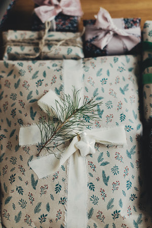 Stylish christmas gifts in festive wrapping paper with fir branch, bows, ribbons, vintage ornaments...