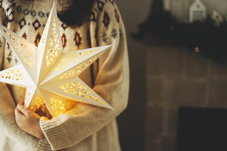 Stylish glowing big christmas star in hands of on background of decorated christmas fireplace with vintage baubles and lights. Merry Christmas! Atmospheric magic winter timeの写真素材