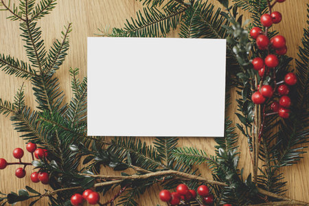 Empty greeting card and fir branches with red berries on wooden table. Christmas card mock up flat...