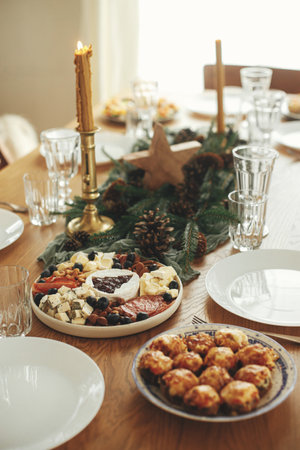 Christmas table setting. Modern cheese platter with cranberry sauce as christmas tree, fir branches and pine cones, candles, appetizers, glasses and cutlery. Food arrangement for holidaysの写真素材