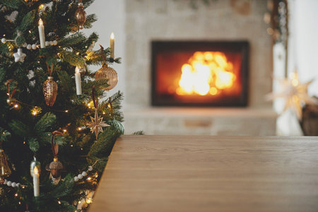 Stylish wooden table against christmas tree with lights and burning fireplace. Christmas festive template and wooden board mock up for product. Christmas background, copy spaceの写真素材