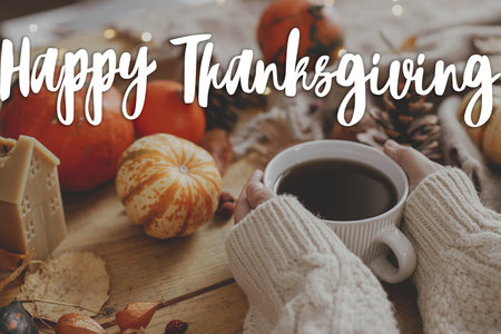 Happy Thanksgiving! Happy thanksgiving text and hands holding warm cup of tea and pumpkins, autumn leaves, cozy scarf on rustic table. Season Greeting card, handwritten sign. Give thanksの写真素材