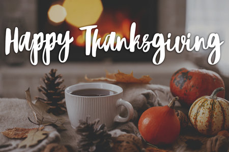 Happy Thanksgiving! Happy thanksgiving text and warm cup of tea, pumpkins, autumn leaves, cozy scarf and lights against fireplace. Season Greeting card, handwritten sign. Give thanksの写真素材