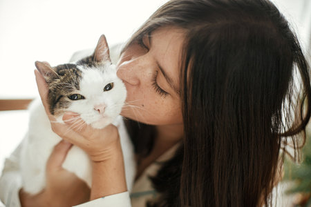 Happy woman in stylish pajamas hugging and kissing adorable cat in festive living room. Merry Christmas! Winter holidays and petの写真素材