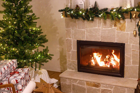 Merry Christmas! Atmospheric Christmas eve, holiday time. Stylish wrapped christmas gifts on arm chair, christmas tree with festive lights and cozy burning fireplace.の写真素材