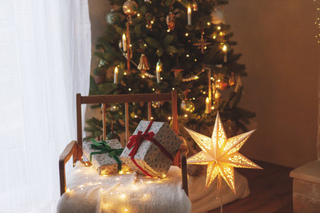 Stylish christmas gifts on background of modern decorated christmas tree with golden lights and illuminated star. Atmospheric christmas eve in scandinavian room. Merry Christmas!の写真素材