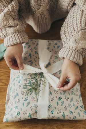 Wrapping christmas gifts. Hands in cozy sweater wrapping stylish present in festive wrapping paper...
