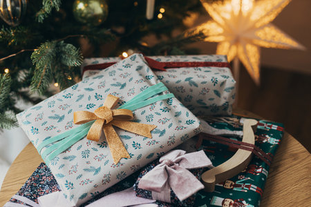 Merry Christmas! Stylish christmas gifts wrapped in festive paper with bows, vintage ornament and toy on wooden table on background of christmas tree lights. Atmospheric winter holidaysの写真素材