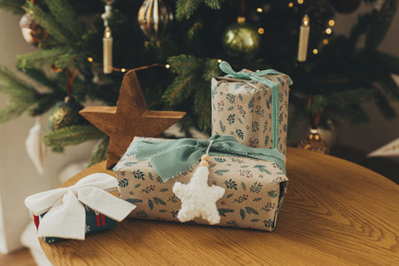 Stylish christmas gifts in festive wrapping paper with bows, vintage ornaments, toy on wooden table on background of christmas tree lights. Happy holidays! Atmospheric christmas eveの写真素材