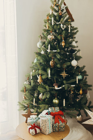 Stylish christmas gifts in festive wrapping paper with bows and vintage ornaments on wooden table on background of golden christmas tree lights.Happy holidays! Atmospheric christmas eveの写真素材