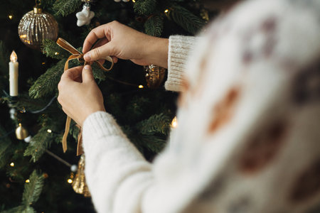 Hands in cozy sweater hanging  modern velvet decoration on tree branch close up. Decorating christmas tree with stylish ribbon. Atmospheric winter holiday tradition, family timeの写真素材