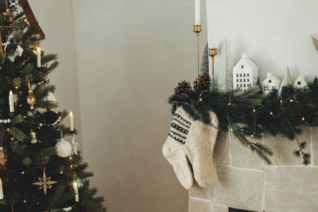 Cozy stockings hanging on mantel in modern farmhouse living room. Rustic christmas fireplace with warm knitted stockings and stylish decoration on fir branches. Atmospheric winter holidayの写真素材