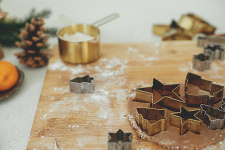 Gingerbread dough with festive golden metal cutters on wooden board with flour, cooking spices, festive decorations in modern white kitchen. Making christmas gingerbread cookiesの写真素材