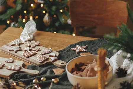 Christmas holiday traditions, atmospheric family time. Gingerbread cookies with icing on rustic wooden table with christmas golden lights. Decorating cookies with sugar frostingの写真素材