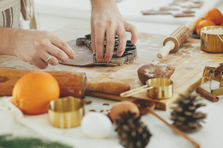 Man making christmas gingerbread cookies close up in modern white kitchen. Hands cutting gingerbread dough with festive golden metal cutters with cooking spices and decorationsの写真素材