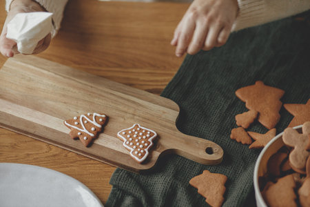 Decorating gingerbread cookies with icing on rustic wooden table close up. Atmospheric Christmas...