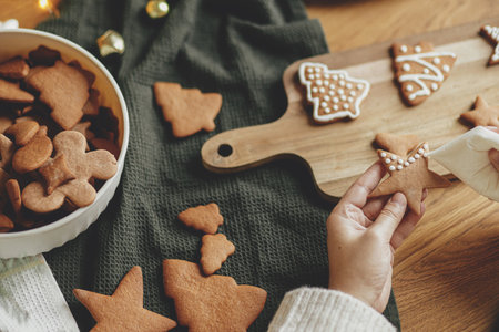 Decorating gingerbread cookies with icing on rustic wooden table top view. Atmospheric Christmas holiday traditions. Hands decorating baked christmas cookies with sugar frosting. Family timeの写真素材