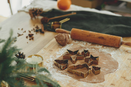 Gingerbread dough with golden cutters, rolling pin, cooking spices and festive decorations on rustic wooden table. Making christmas gingerbread cookies, atmospheric holiday timeの写真素材