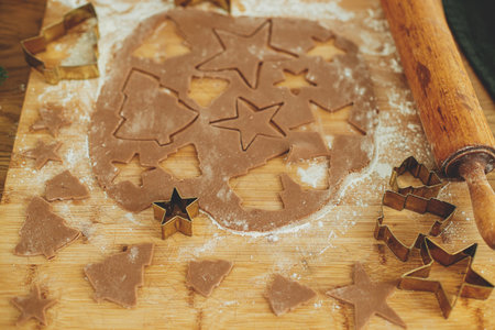 Making christmas gingerbread cookies, atmospheric holiday time. Gingerbread dough with golden cutters, rolling pin, festive decorations on rustic wooden tableの写真素材