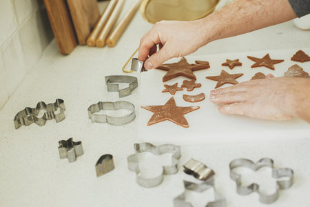 Man making christmas gingerbread cookies close up in modern white kitchen. Hands cutting gingerbread dough with festive metal cutters with cooking spices and decorationsの写真素材