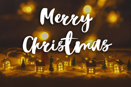 Merry Christmas text on cozy christmas miniature village with lights bokeh in evening. Happy Holidays! Season's greeting card. Handwritten signの写真素材