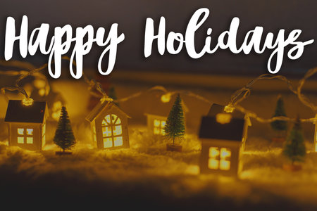 Happy Holidays text on cozy christmas miniature village with lights bokeh in evening. Merry Christmas. Season's greeting card. Handwritten signの写真素材