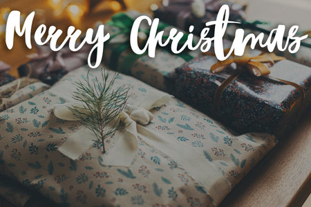Merry Christmas text on stylish christmas gift with fir branch and  festive vintage ornaments on wooden table. Happy Holidays! Season's greeting card. Handwritten signの写真素材