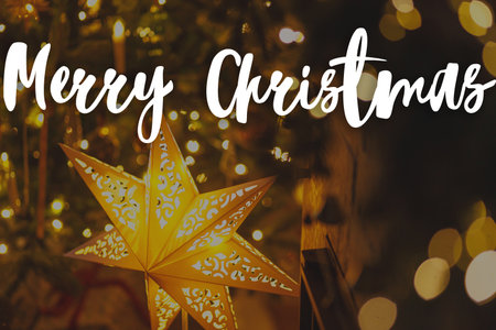 Merry Christmas text on stylish christmas illuminated star and christmas tree with golden lights in evening. Happy Holidays! Season's greeting card. Handwritten signの写真素材