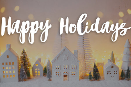 Happy Holidays text on stylish little white houses and trees, snowy christmas miniature village with golden lights. Merry Christmas. Season's greeting card. Handwritten signの写真素材