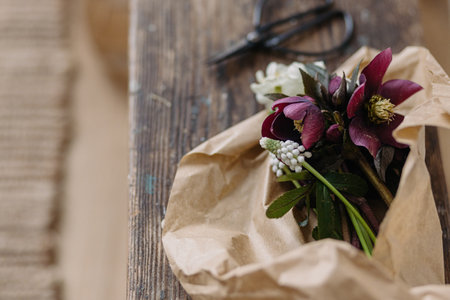Beautiful spring bouquet in craft paper and scissors on rustic wooden background. First spring flowers helleborus, muscari, daffodils. Floral simple rural decorの写真素材