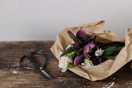 Beautiful spring bouquet in craft paper and scissors on rustic wooden background. First spring flowers helleborus, muscari, daffodils. Floral simple rural decorの写真素材