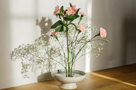 Beautiful pink and white flowers in bowl on rustic background. Tender floral composition on kenzan or flower pin in sunlight. Modern flower arrangementの写真素材