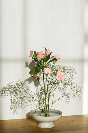 Beautiful pink and white flowers in bowl on rustic background. Tender floral composition on kenzan or flower pin in sunlight. Modern flower arrangementの写真素材