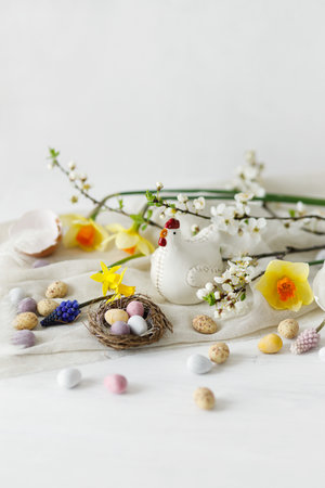 Easter still life. Colorful easter chocolate eggs in nest, spring flowers, chicken figurine composition on white wooden table. Space for text. Happy Easter! Seasons greetingsの写真素材