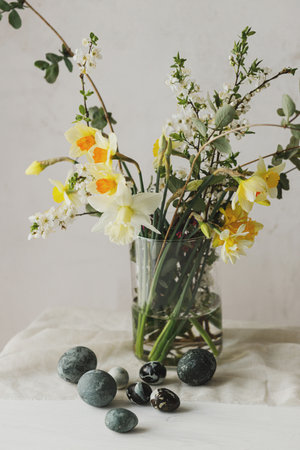 Stylish easter eggs and spring flowers bouquet on rustic wooden table. Easter modern simple decor, natural painted marble eggs. Seasons greetings. Happy Easter!の写真素材
