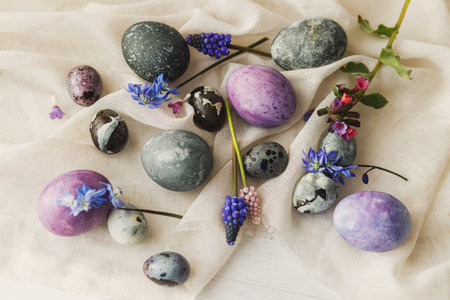 Stylish easter eggs, gentle spring flowers and linen cloth on rustic white table. Space for text. Happy Easter! Natural painted marble and purple eggs. Seasons greetingsの写真素材