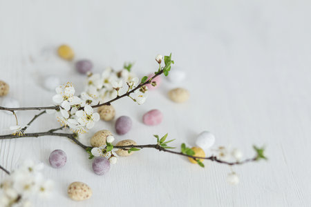Happy Easter! Stylish easter chocolate eggs and gentle spring flowers on white rustic wooden table. Easter modern simple banner, space for text. Seasons greetingsの写真素材