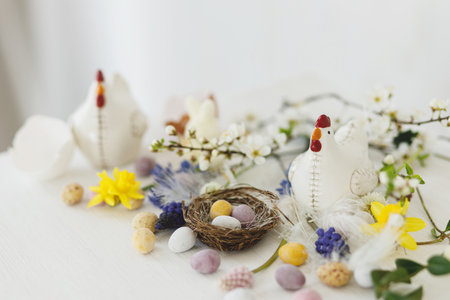 Happy Easter! Stylish easter chocolate eggs in nest, spring flowers, chicken figurine on white rustic wooden table. Easter modern simple banner, space for text. Seasons greetingsの写真素材