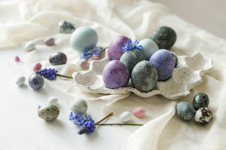Stylish easter eggs in modern tray, gentle spring flowers and linen cloth on rustic white table....