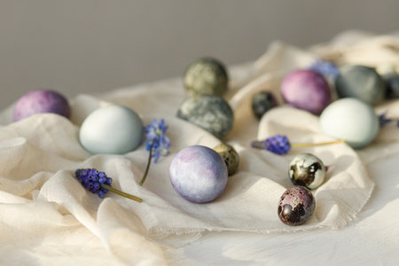 Stylish easter eggs, gentle spring flowers and linen cloth on rustic white table in sunlight. Space for text. Happy Easter! Natural painted marble and purple eggs. Seasons greetingsの写真素材