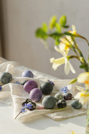 Stylish easter eggs, gentle spring flowers and linen cloth on rustic white table in sunlight. Space for text. Happy Easter! Natural painted marble and purple eggs. Seasons greetingsの写真素材