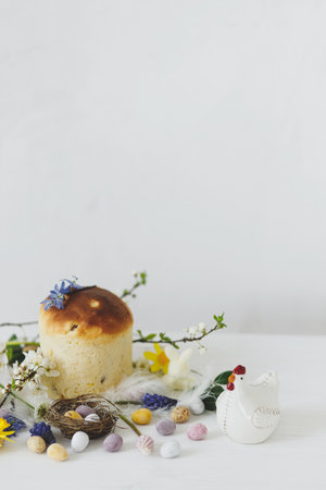 Colorful easter chocolate eggs in nest, spring flowers, traditional bread composition on rustic white wooden table. Space for text. Happy Easter! Seasons greetingsの写真素材