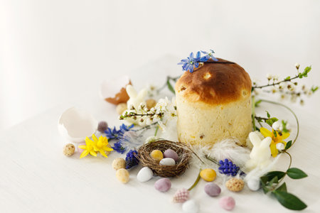 Happy Easter! Stylish easter chocolate eggs in nest, spring flowers, traditional bread on rustic white wooden table. Easter modern simple banner, space for text. Seasons greetingsの写真素材