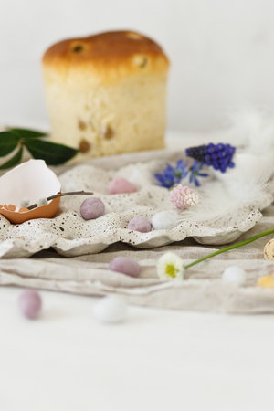 Colorful easter chocolate eggs, easter bread, spring flowers and linen cloth on rustic wooden table. Easter modern simple decoration and homemade traditional cake. Happy Easter!の写真素材