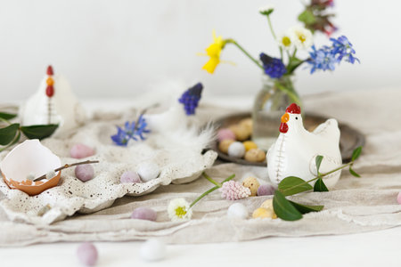 Happy Easter! Stylish easter chocolate eggs, spring flowers, chicken figurines and linen cloth on rustic wooden table. Space for text. Easter modern simple decorationの写真素材