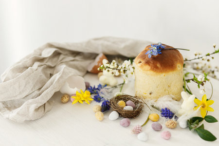 Colorful easter chocolate eggs in nest, spring flowers, traditional bread composition on rustic white wooden table. Space for text. Happy Easter! Seasons greetingsの写真素材