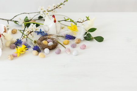 Happy Easter! Stylish easter chocolate eggs in nest, spring flowers, chicken figurine on white rustic wooden table. Easter modern simple banner, space for text. Seasons greetingsの写真素材