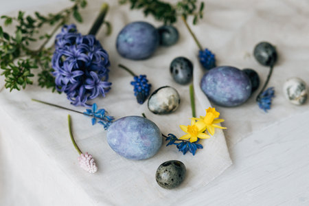 Stylish easter eggs and spring flowers on rustic wooden table. Happy Easter! Natural dye marble and blue eggs, purple hiacynt blossoms and daffodils. Minimal still life.の写真素材